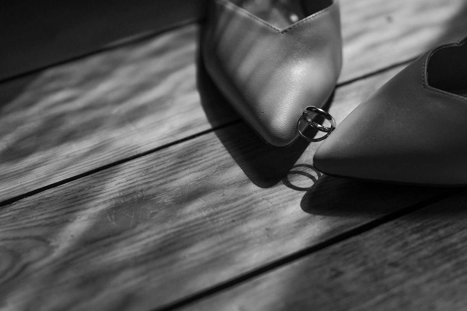 Photographie en noir et blanc des alliances posées sur le bout des talons de la mariée