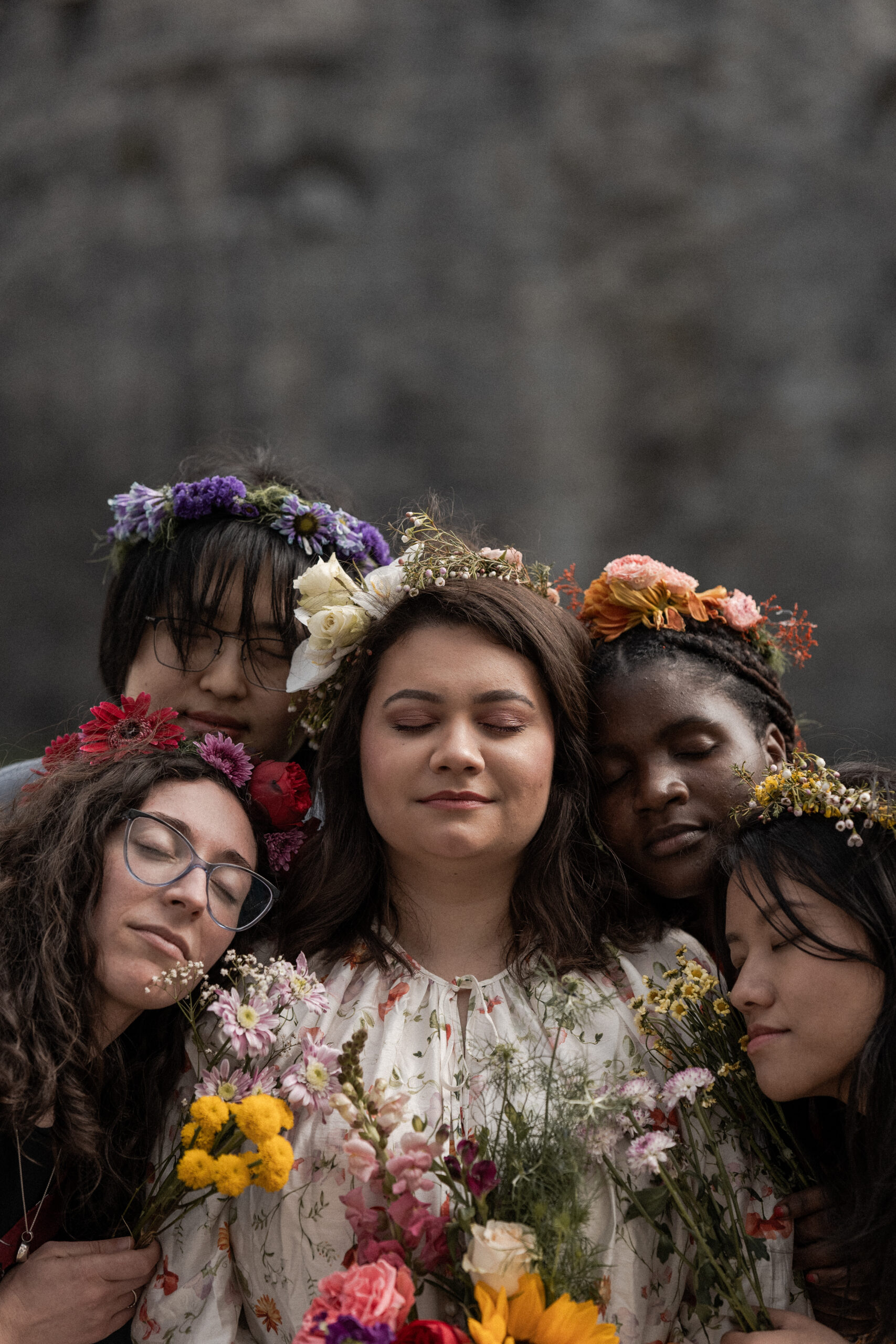 Photographie de 5 femmes lors d'un EVJF, elles sont toutes autour de la future mariée, elles ferment toutes les yeux et elles portent toutes une couronne de fleurs dans leurs cheveux