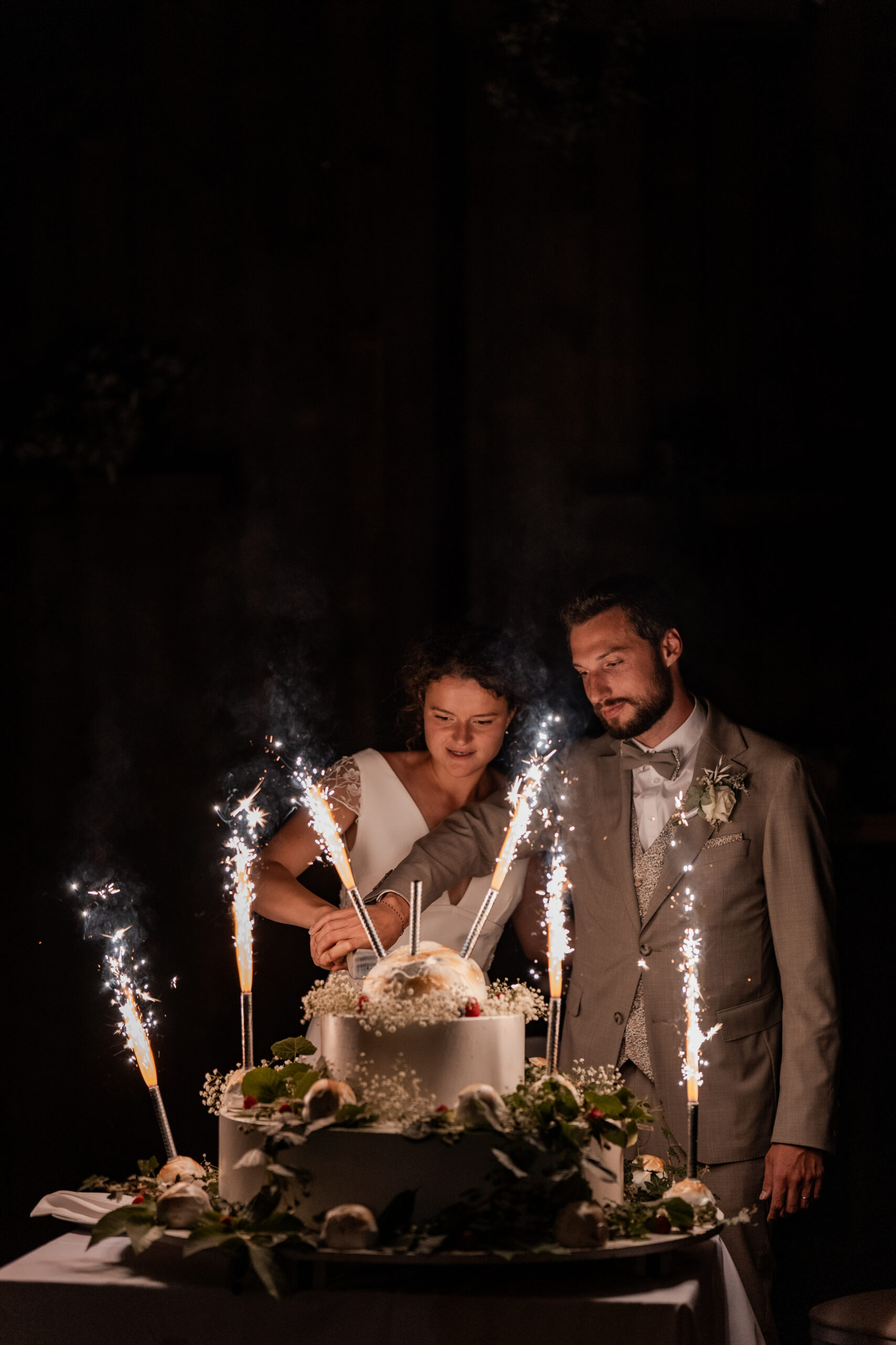 Photographie d'un couple de mariés qui coupent leur gâteau de mariage dans la pénombre