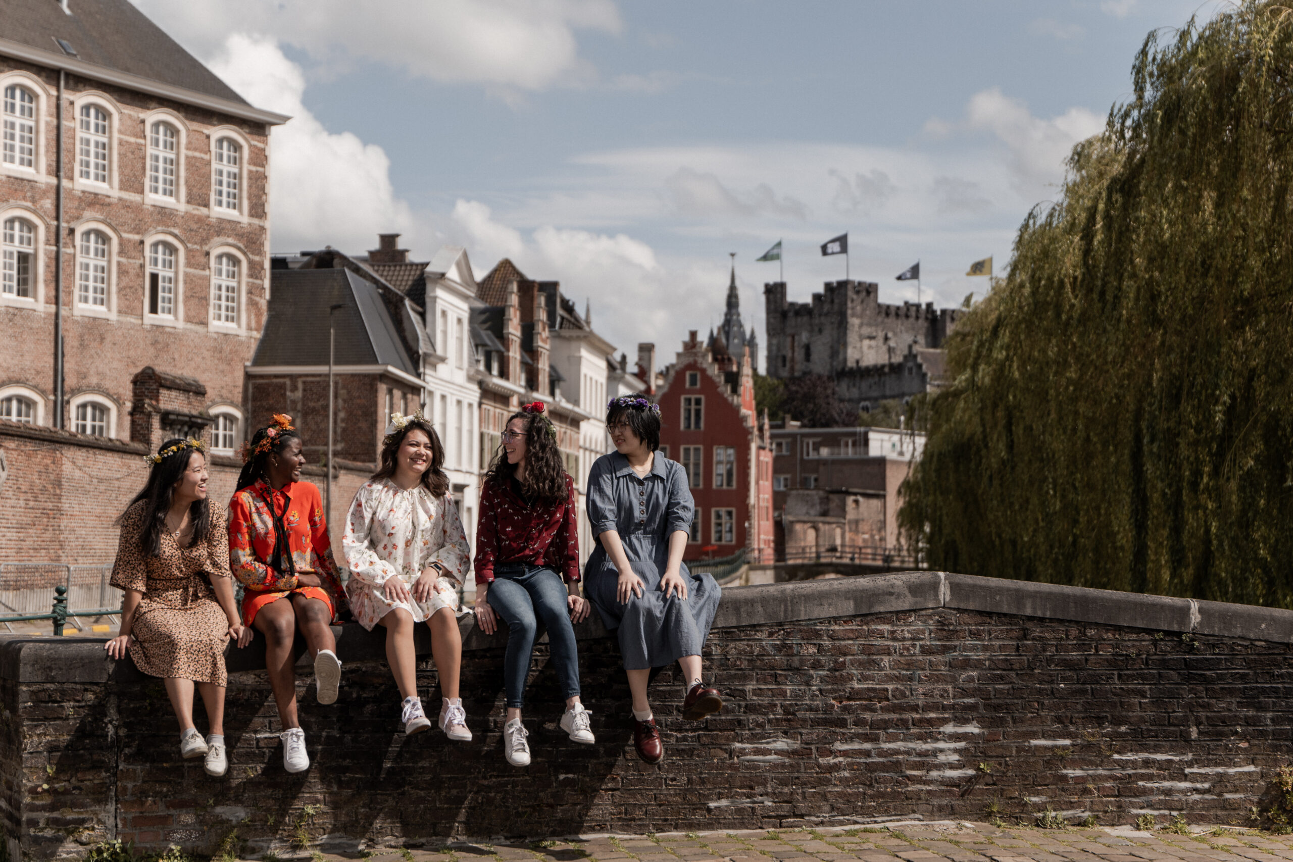 Photographie d'un groupe d'amies assises sur un petit muret et souriant tout en se regardant les unes les autres, les château de Gravensteen en fond lors d'un EVJF à Gand en Belgique