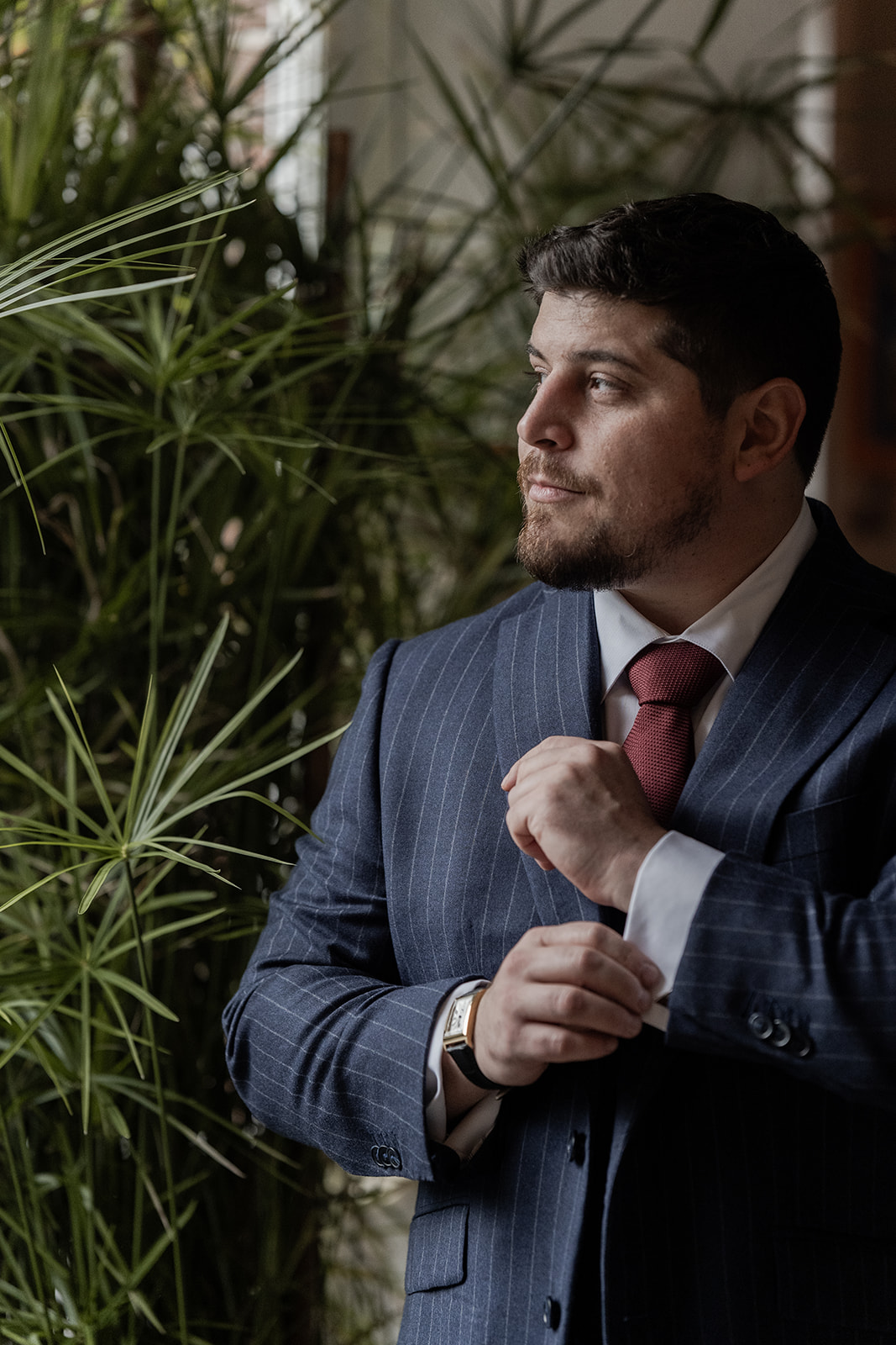 Photographie d'un portrait d'un marié qui regarde vers le côté tout en refermant les boutons de manchettes de sa chemise lors des préparatifs de son mariage