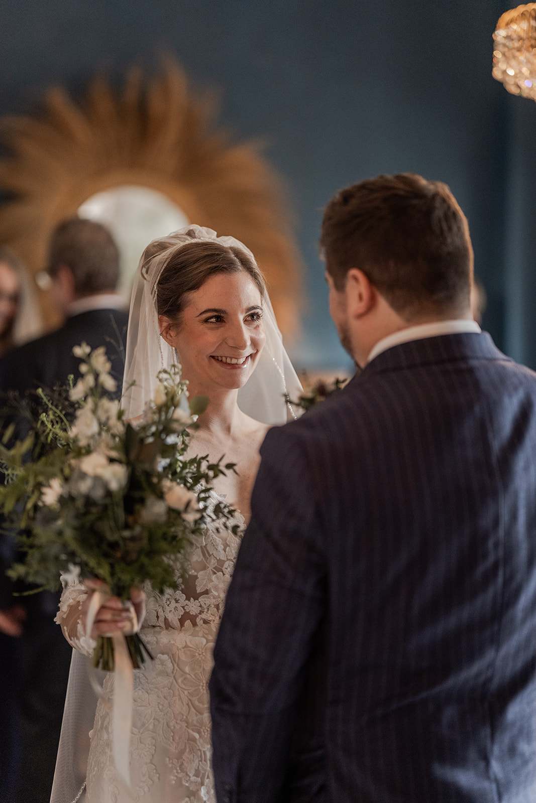 Photographie d'une mariée qui regarde en souriant son mari qui est de dos et qu'elle vient de découvrir lors des préparatifs de son mariage