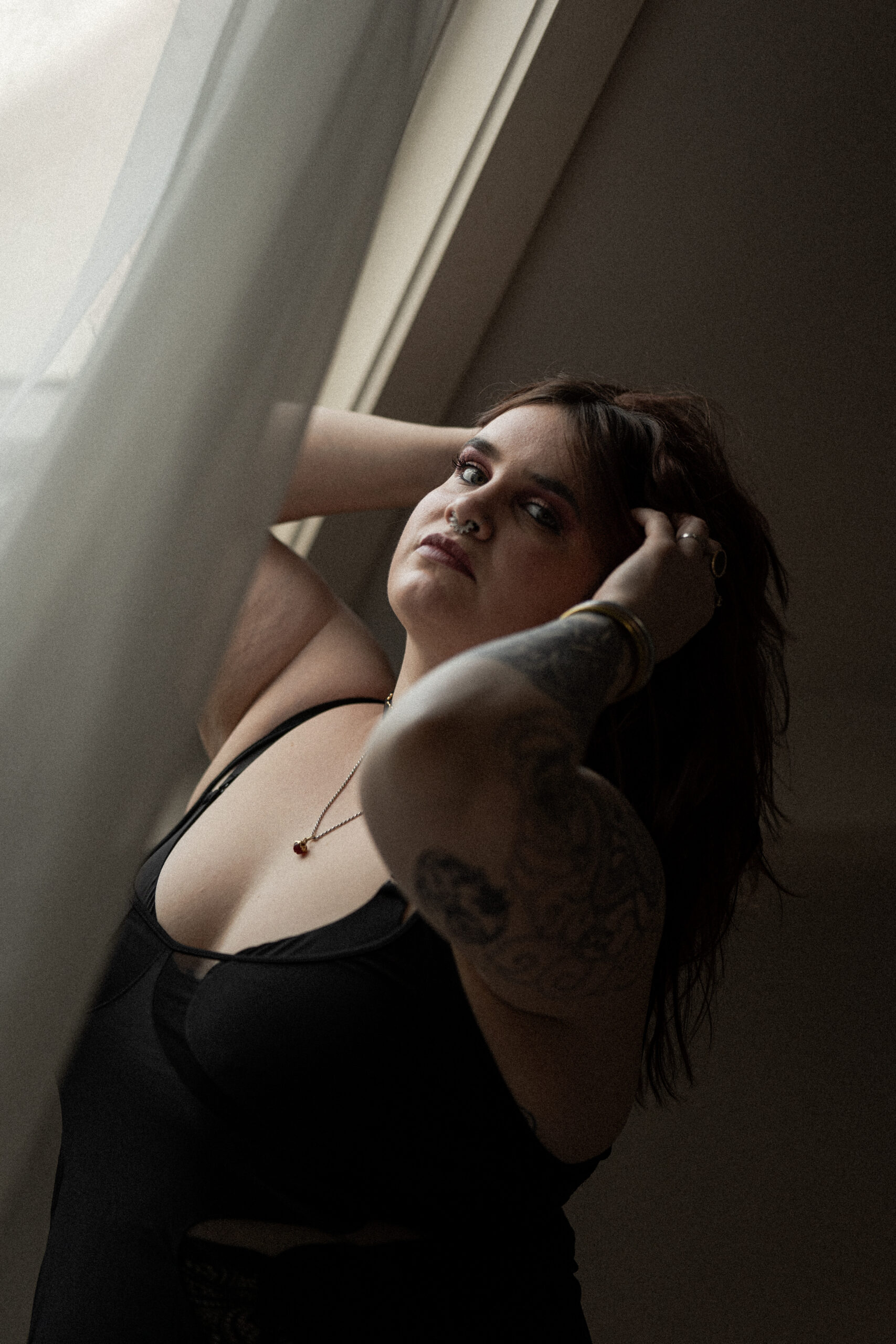 Photographie d'une femme près d'une fenêtre qui a ses mains dans ses cheveux