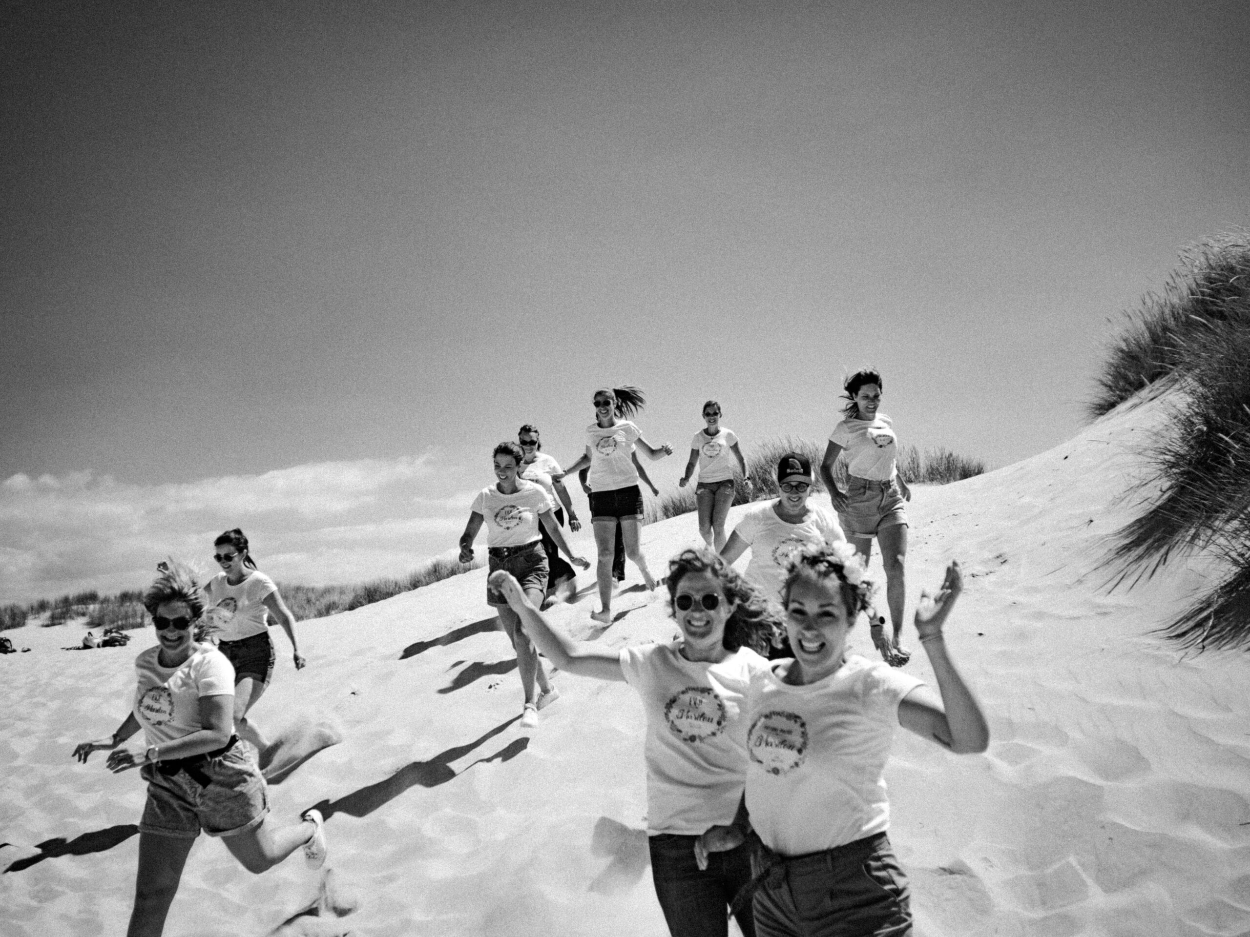 Photographie en noir et blanc d'un groupe d'amies dévalant l dune de sable de la plage du Touquet-Paris-plage