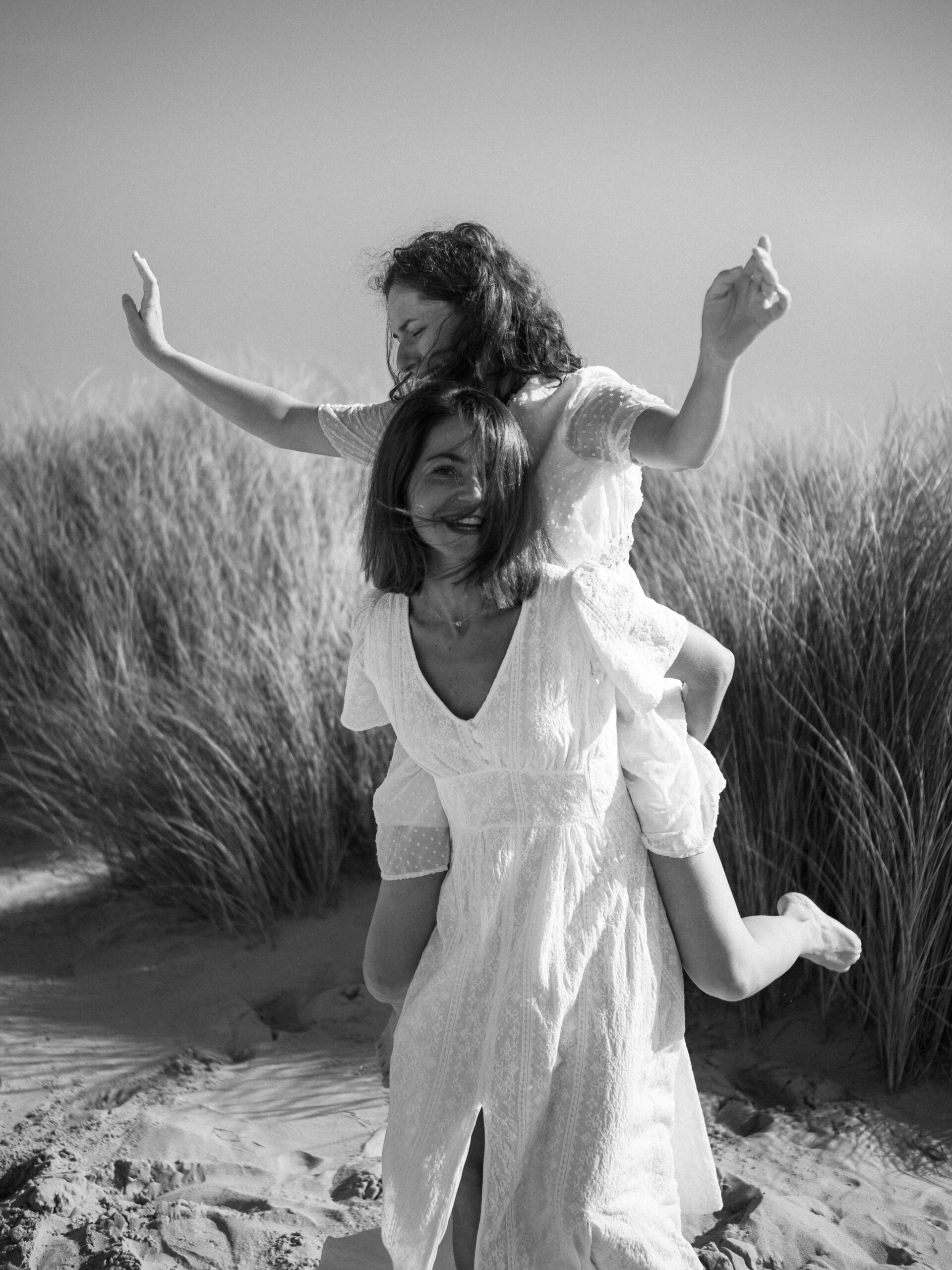 Photographie en noir et blanc d'une femme portant son amie sur le dos dans une dune de sable de la plage du Touquet-Paris-plage lors d'un EVJF