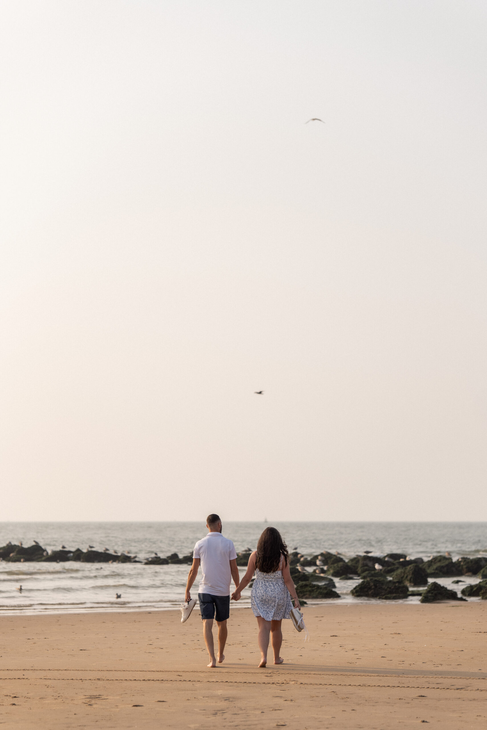 Photographie d'un couple de futurs mariés marchant sur le sable de la plage d'Ostende vers la mer lors d'une séance photo de couple