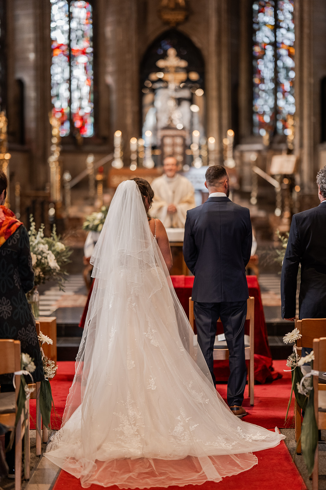 Photographie d'un couple de mariés devant l'autel et le prêtre entourés de leurs invités dans l'église d'Ostende lors de leur cérémonie religieuse de leur mariage