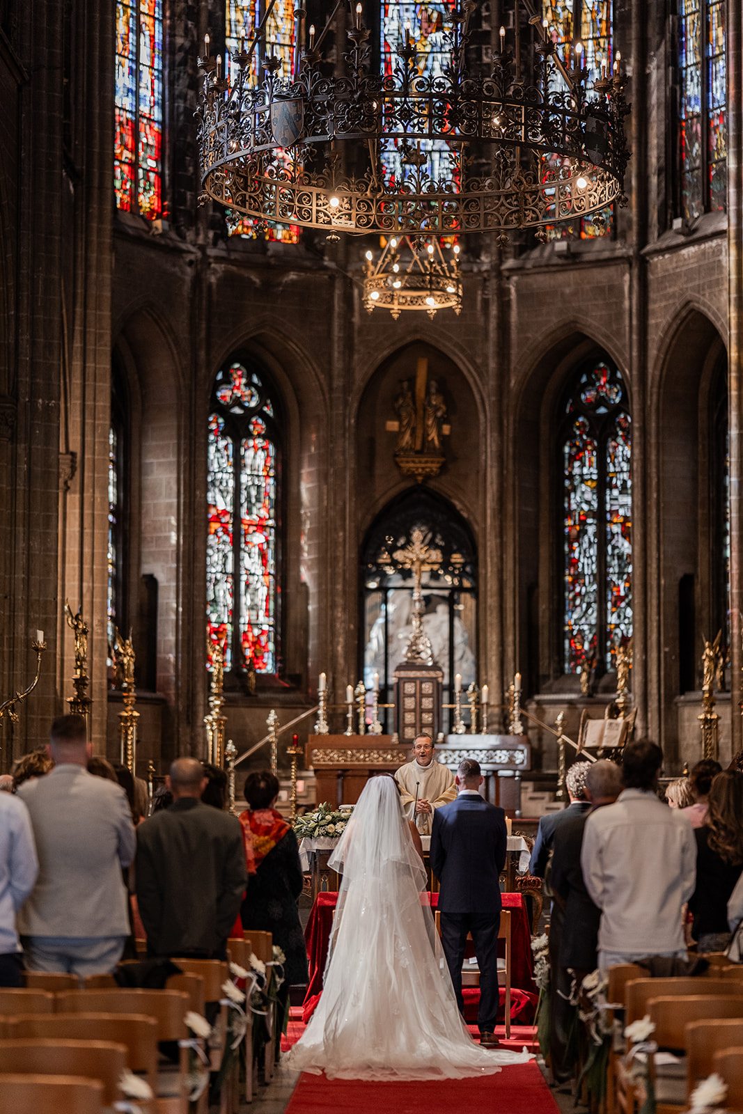 Photographie d'un couple de mariés devant l'autel et le prêtre entourés de leurs invités dans l'église d'Ostende lors de leur cérémonie religieuse de leur mariage