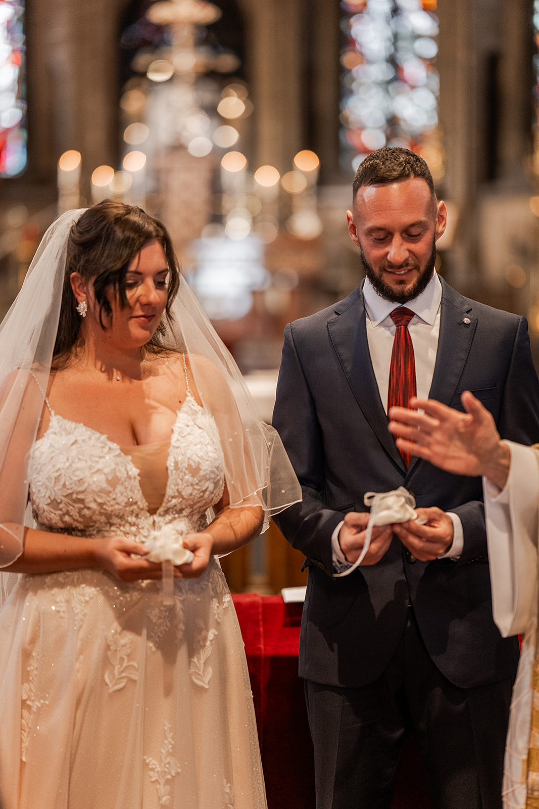 Photographie d'un couple de mariés tenant leur alliance sur leurs coussins et souriant dans l'église d'Ostende lors de leur cérémonie religieuse de leur mariage